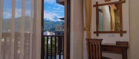 A room with a wooden desk, a chair, a mirror, and a view of mountains through a glass door.