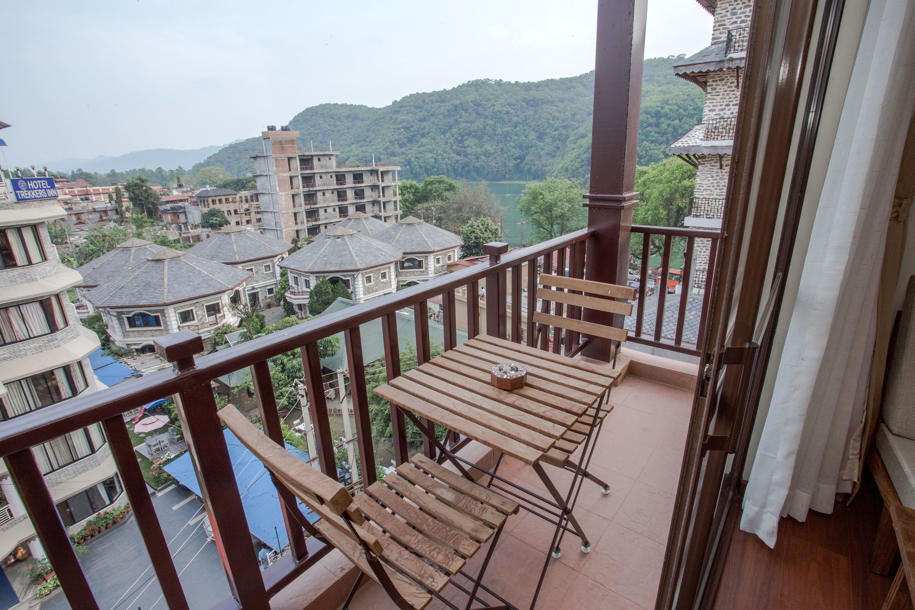 Un balcon agrémenté de meubles en bois, avec vue sur une ville, ses bâtiments et une montagne en arrière-plan.