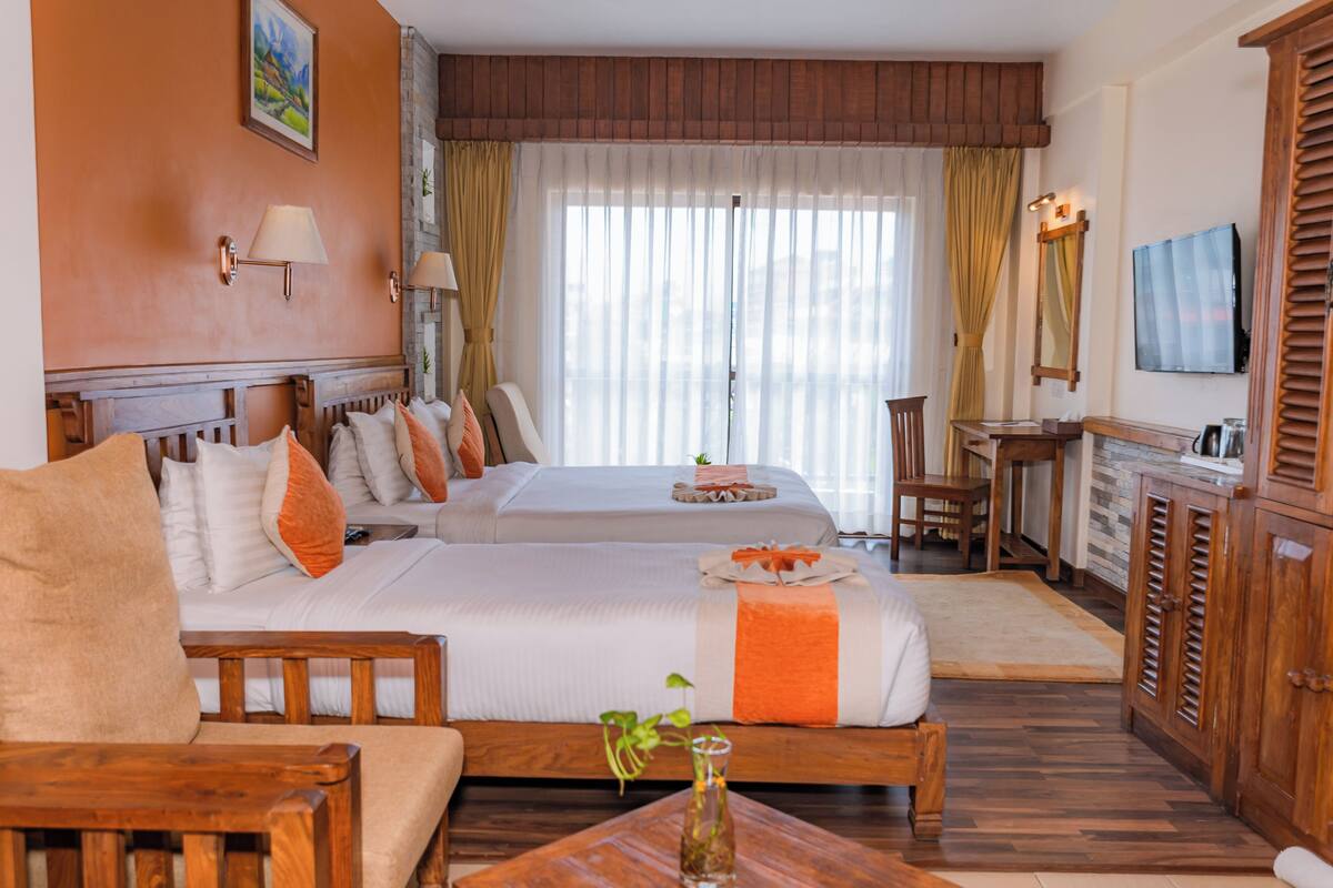 A hotel room with two beds, a wooden headboard, a desk, a TV, and a cabinet.