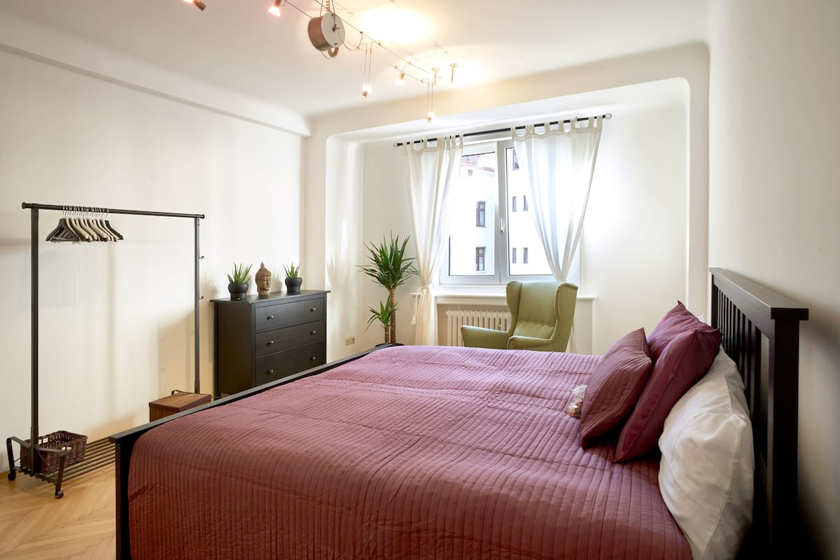 A bedroom with a large bed, a wardrobe, a radiator, and a window with curtains.