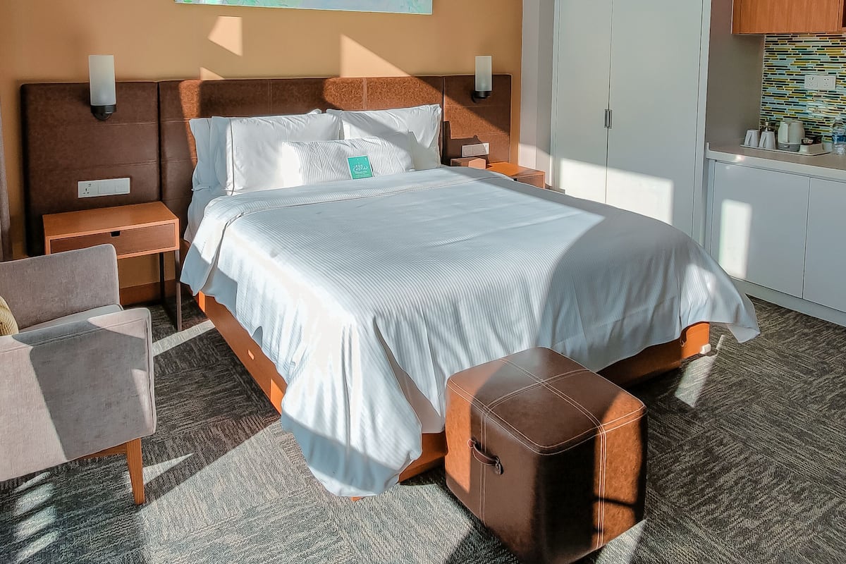 A hotel room with a large bed, a nightstand, a chair, a small stool, a map on the wall, and a wardrobe.