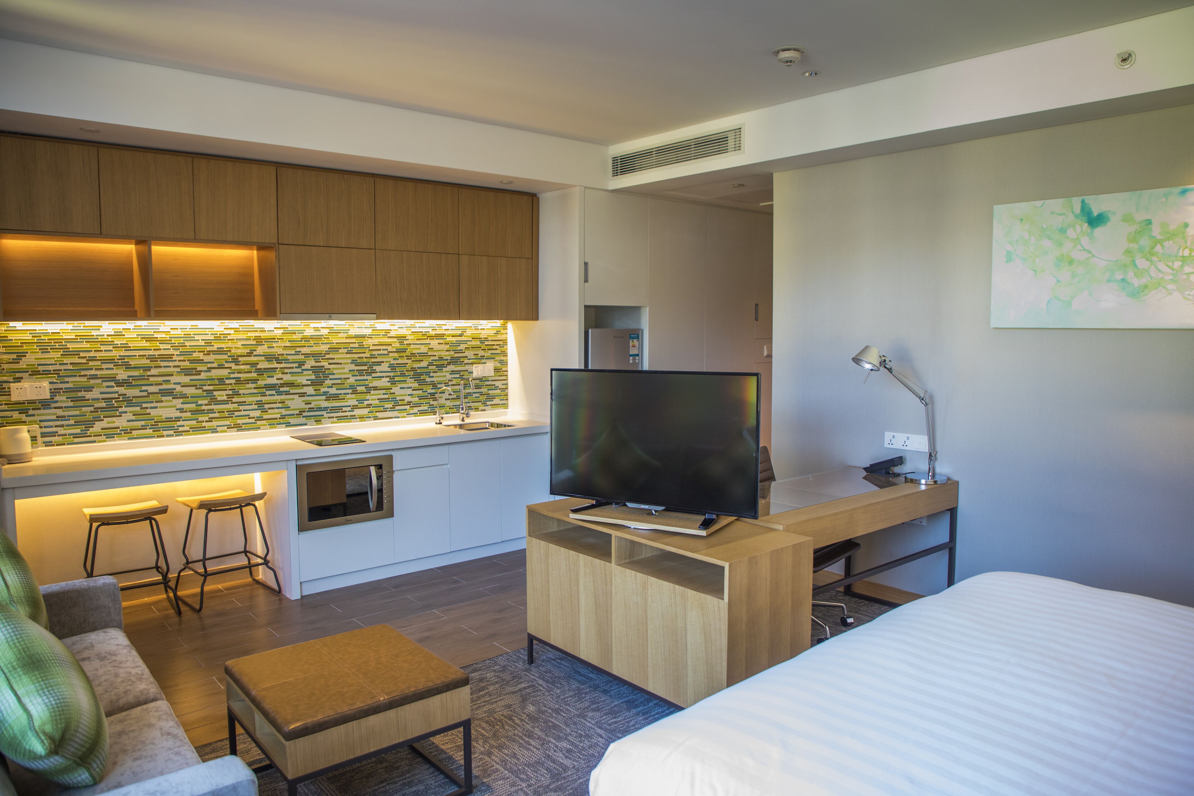 Una habitación de hotel moderna con kitchenette, una televisión de pantalla plana, un escritorio, un sofá cómodo y una cama.