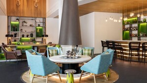 A modern lounge area with a central round table, comfortable seating, a bar with green accents, and a unique conical light fixture. - Element Chongli (Zhangjiakou)