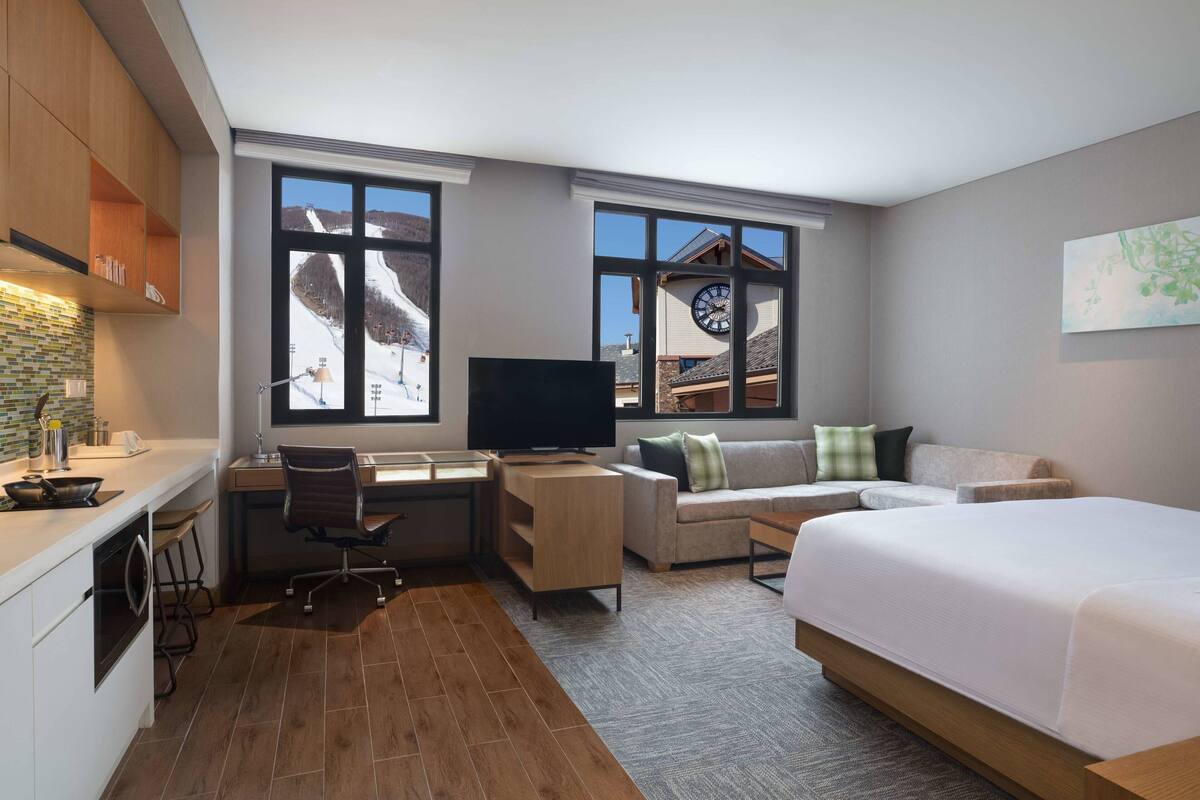 A modern hotel room with a large bed, a desk with a computer, a sofa, and a TV.