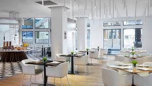 A modern dining area with white chairs and tables, a buffet with various food items, and large windows offering views of the city. - Element Chongli (Zhangjiakou)