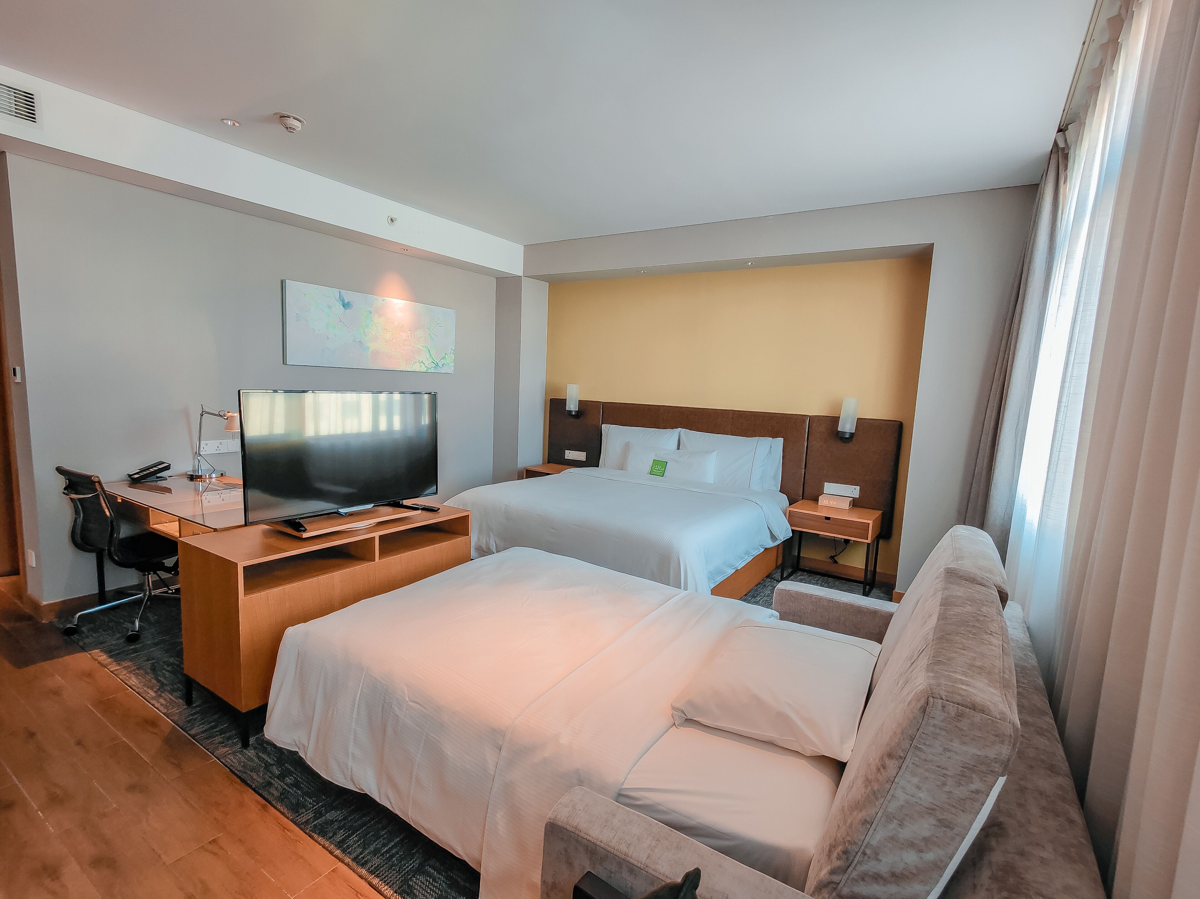 A hotel room with a bed, a desk with a TV, a chair, and a couch.