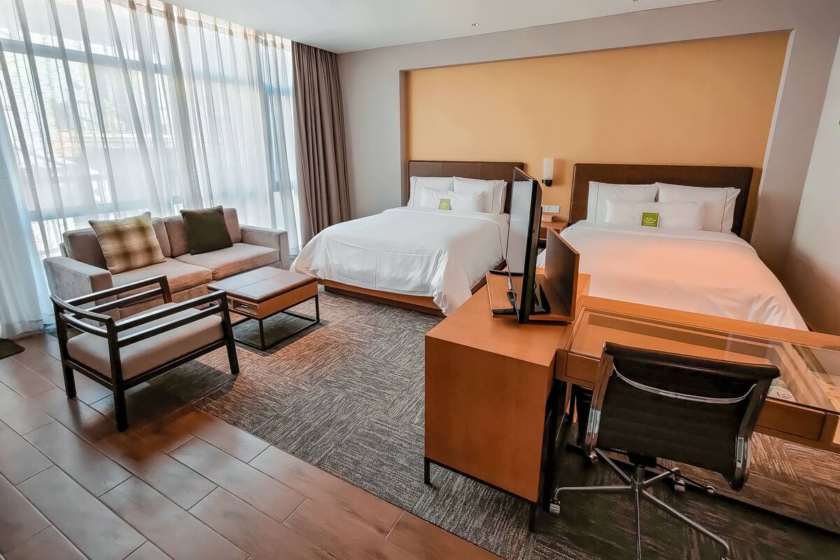 A hotel room with two beds, a sofa, a desk, and a chair.