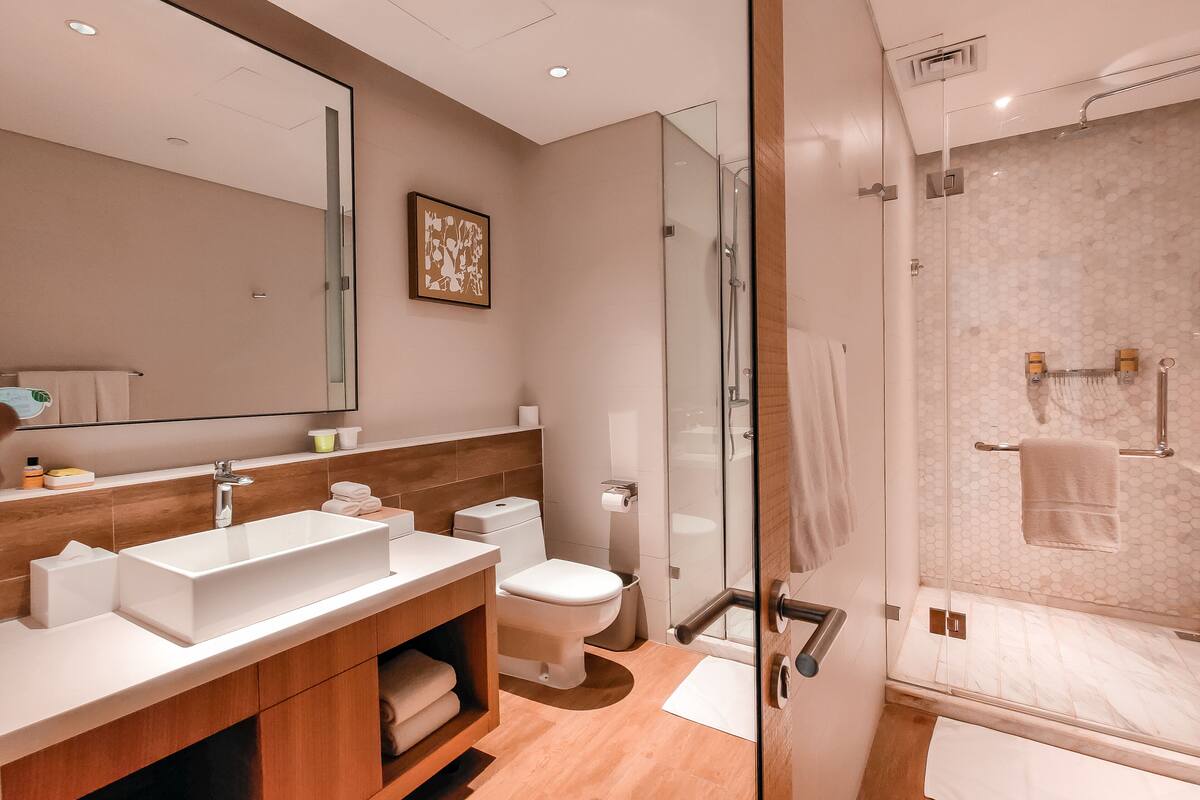 A modern bathroom with a large mirror, a sink, a toilet, and a glass-enclosed shower area.