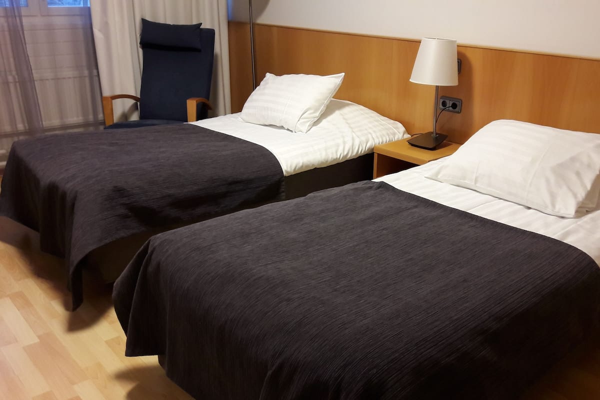 Two single beds with dark and white bedding, a wooden headboard, a nightstand with a lamp, and a chair.