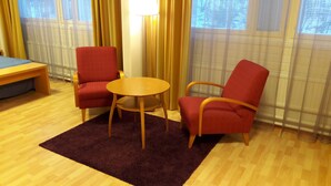 Um quarto com duas cadeiras vermelhas, uma mesa redonda de madeira, um sofá azul e uma luminária.