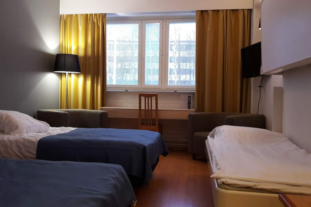 A hotel room with two single beds, a desk, a chair, a TV, and a window with curtains.