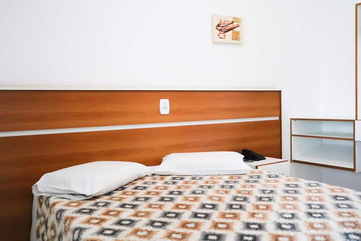 Una cama individual con una colcha estampada, un cabecero de madera y una mesita de noche con lámpara.