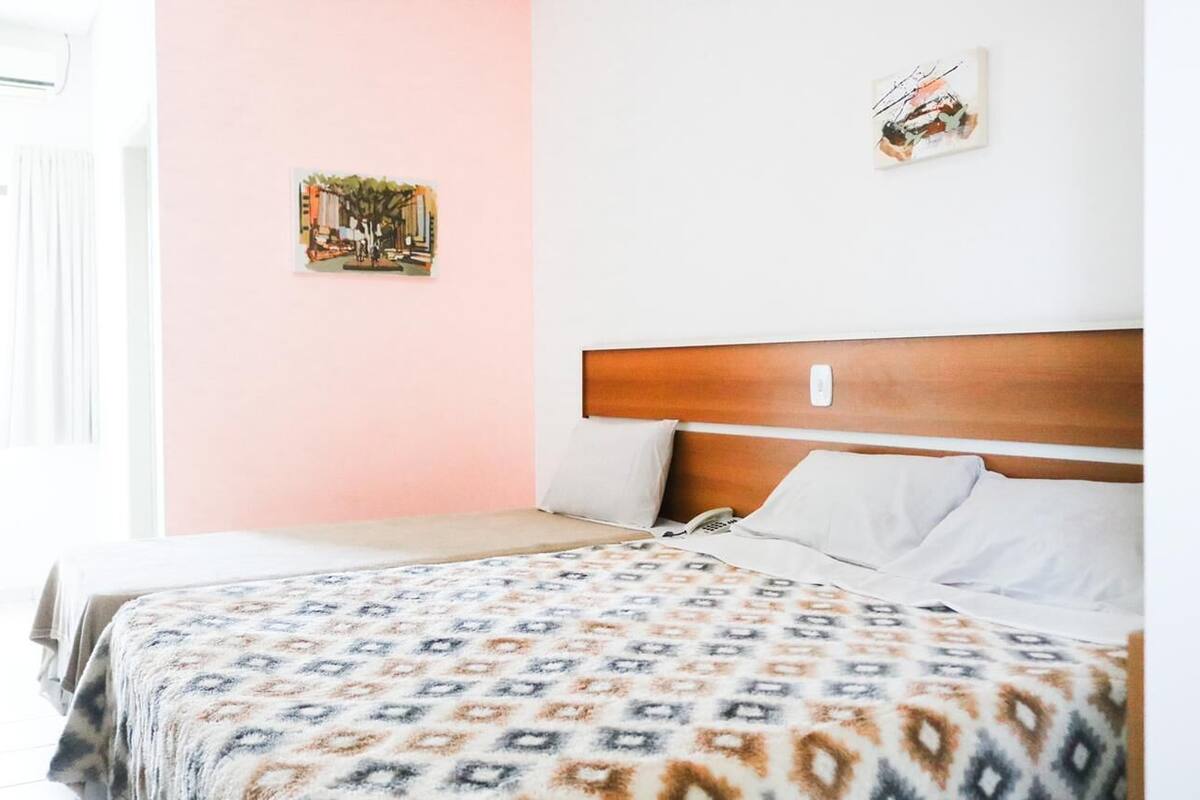 Una habitación de hotel con una cama, cabecera de madera, colcha estampada y dos obras de arte en la pared.