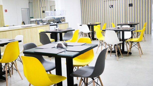 Un comedor moderno con sillas amarillas y blancas, mesas negras y una pared a rayas.