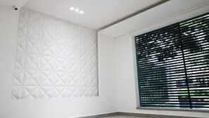 Una habitación con una pared de diseño geométrico, una ventana con persianas horizontales y luces empotradas en el techo.