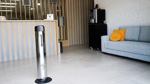 Zona de recepción con pared a rayas, mostrador de recepción, un armario negro, un sofá gris con un cojín naranja y un objeto metálico en el suelo.