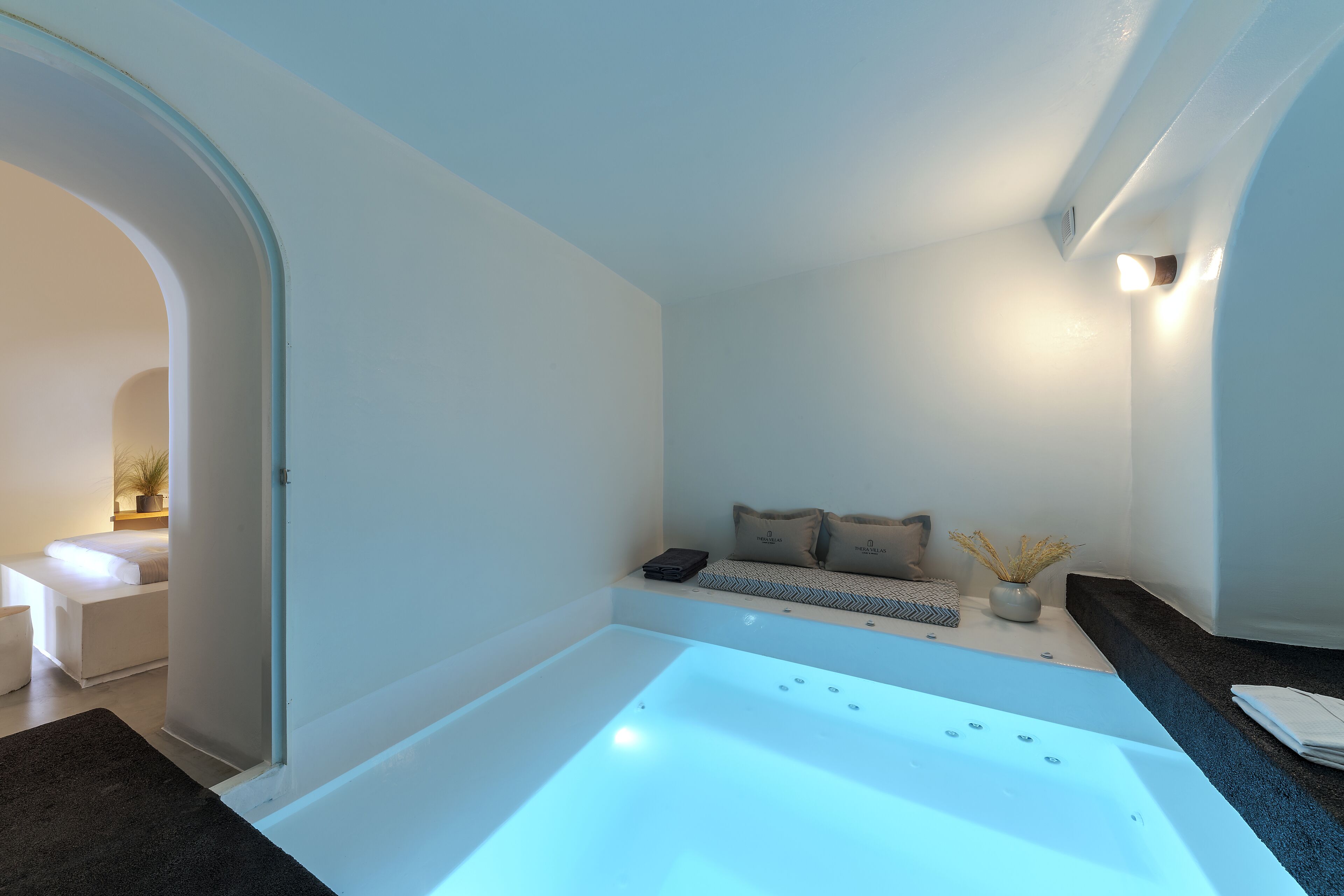 A modern bathroom with a large bathtub, a seating area with cushions, and a small table with a vase.