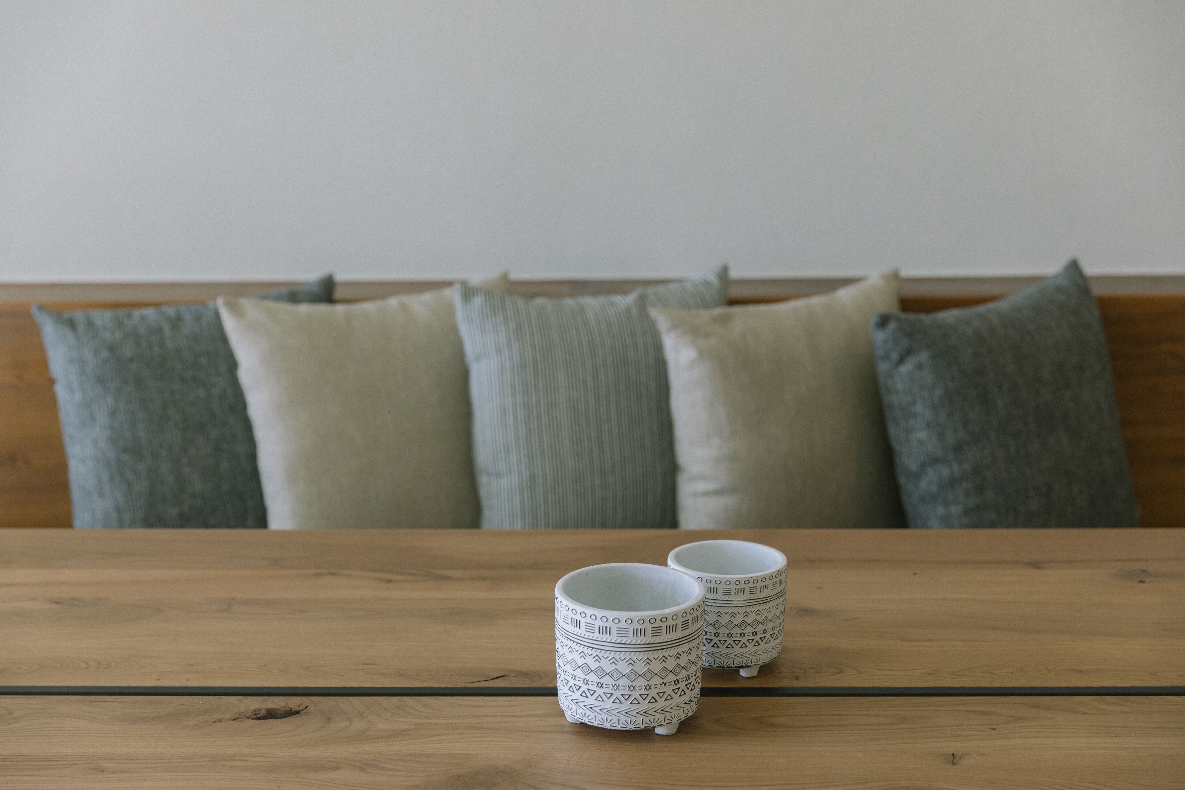 Two patterned cups on a wooden table with a sofa and pillows in the background.