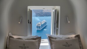 A window view of a cruise ship from a hotel room with two pillows labeled "Thera Villas." - Thera Villas (Santorini)