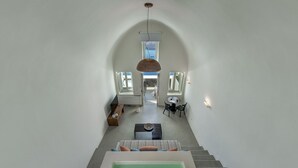 A spacious interior with a central staircase leading to a balcony, a seating area with a table, and a view of the outdoors. - Thera Villas (Santorini)