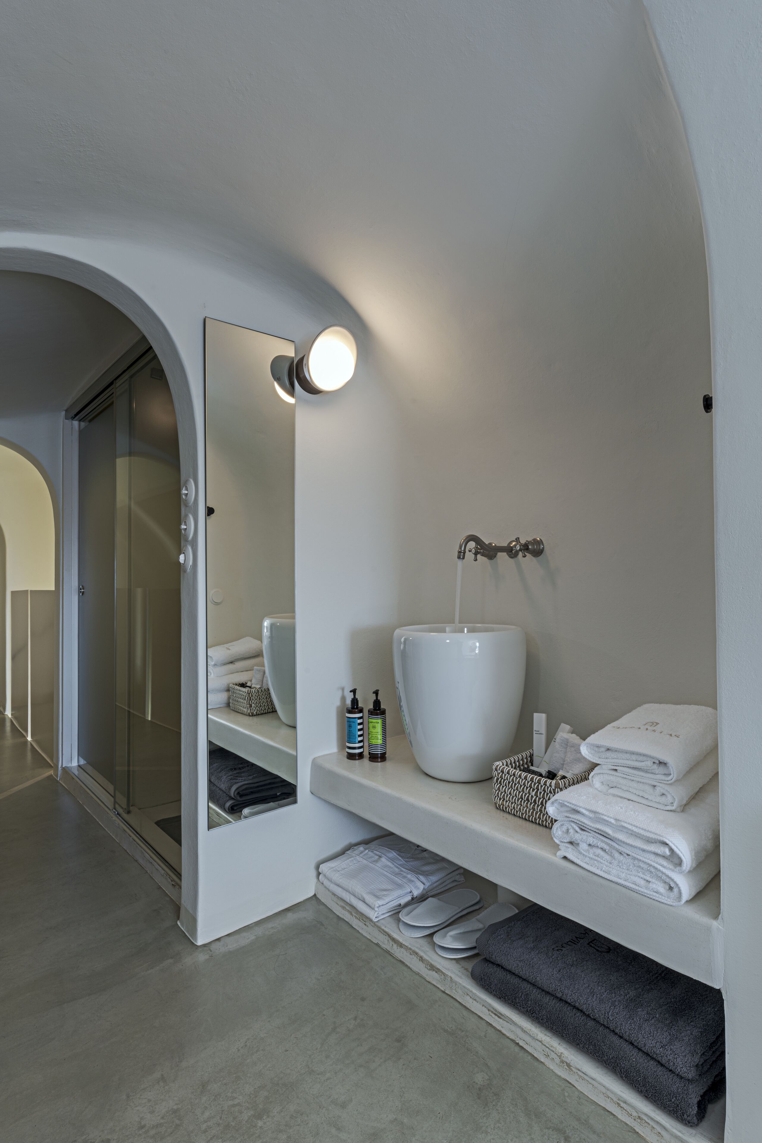 A modern bathroom with a large mirror, a white sink, and neatly folded towels on shelves.
