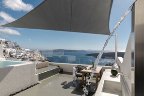A rooftop terrace with a view of the sea and a white building in the background. - Thera Villas (Santorini)