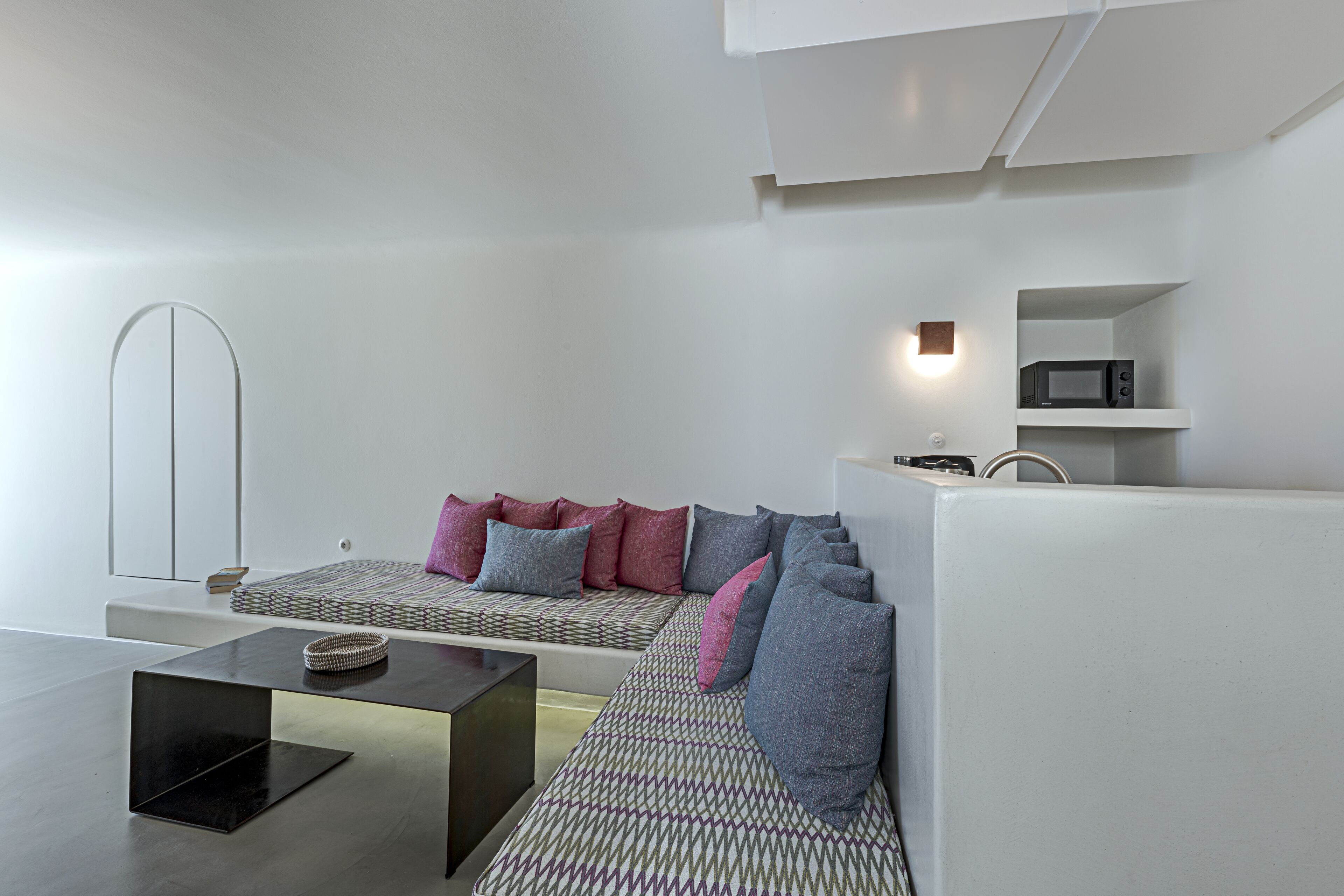 A modern living room with a sofa, a coffee table, and a microwave on a shelf.