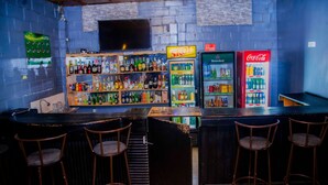 Zona de bar con estantes llenos de botellas de licor, un refrigerador Heineken y un enfriador de Coca-Cola.