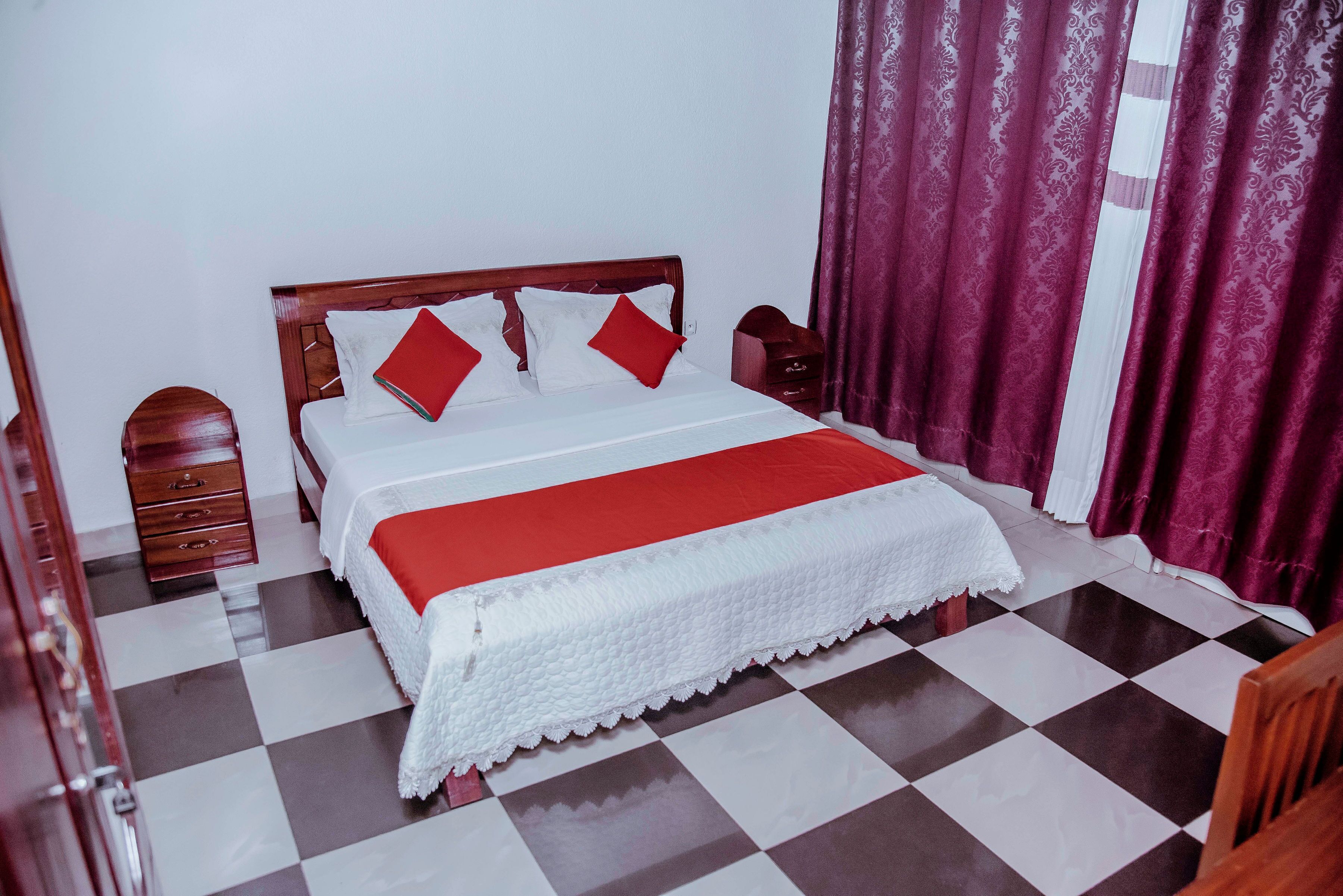 Quarto bem arrumado com chão xadrez, estrutura de cama em madeira e colcha vermelha e branca.