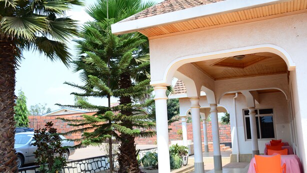 Un espacio exterior cubierto con un muro de piedra, palmeras y un edificio de ladrillo al fondo.