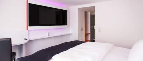 A modern hotel room with a large bed, a flat-screen TV mounted on the wall, a desk with a chair, and a walk-in closet.