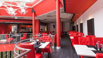 Un restaurante moderno con decoración roja y blanca, con mesas y sillas altas, una barandilla de cristal y un nivel superior.
