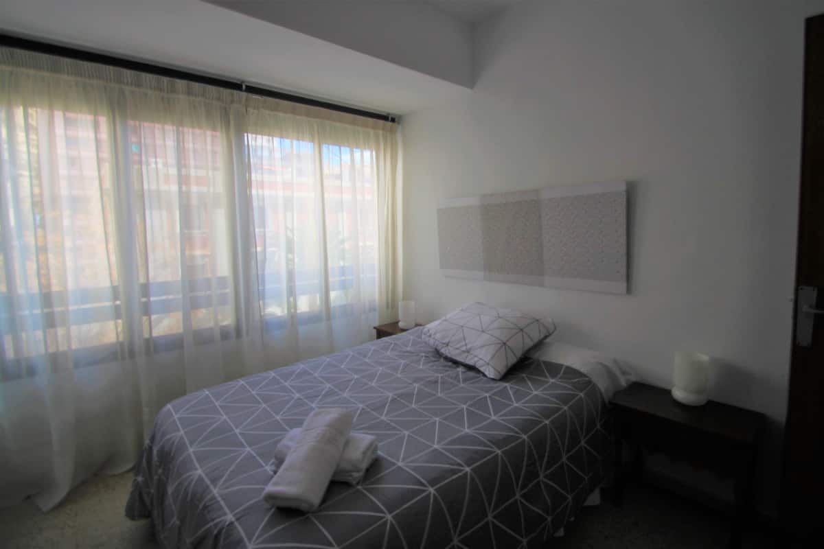 Un dormitorio con cama, cortinas, mesita de noche y lámpara de pared.