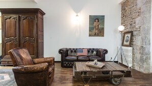 A room with a leather armchair, a sofa with an American flag pillow, a wooden coffee table, and a stone wall. - O'Lodge By Arvor Hotel (Dinan)