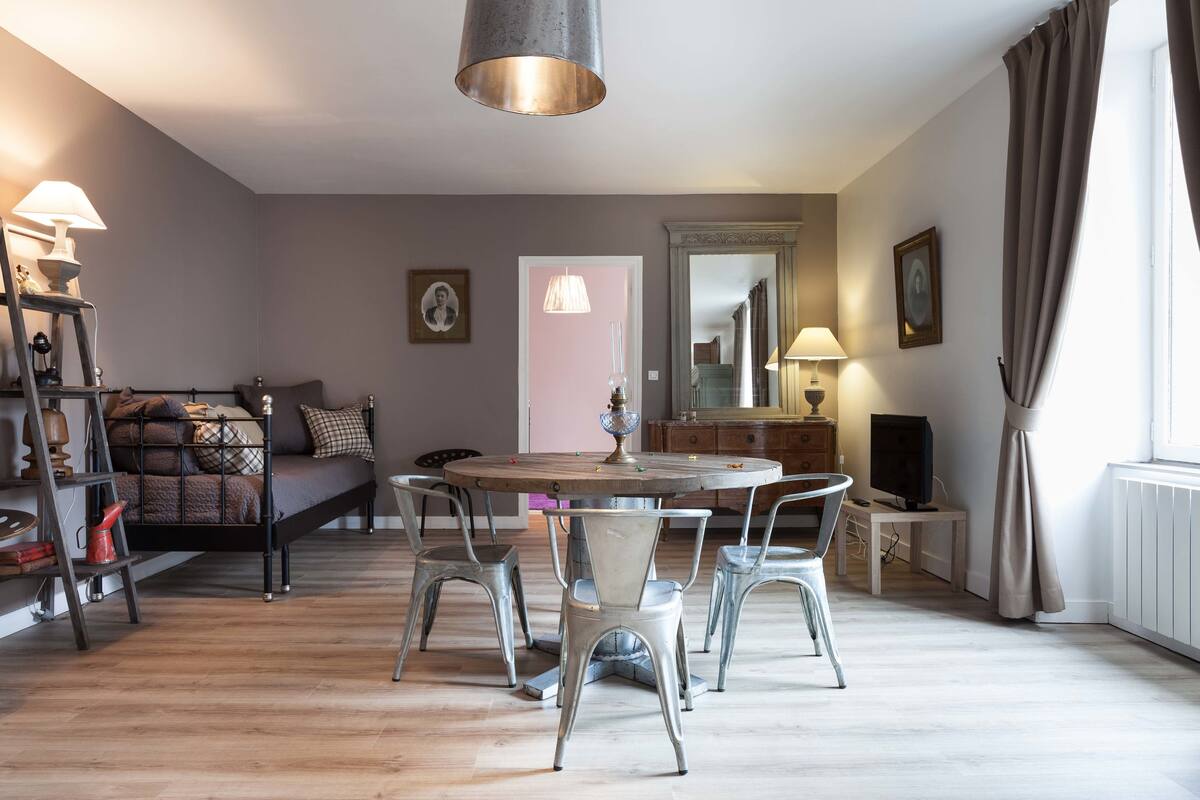 A cozy room with a round dining table, metal chairs, a sofa, a ladder, and a TV.