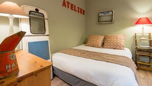 A bedroom with a bed, two pillows, a wooden nightstand, a lamp, and a vintage-style wall decoration. - O'Lodge By Arvor Hotel (Dinan)