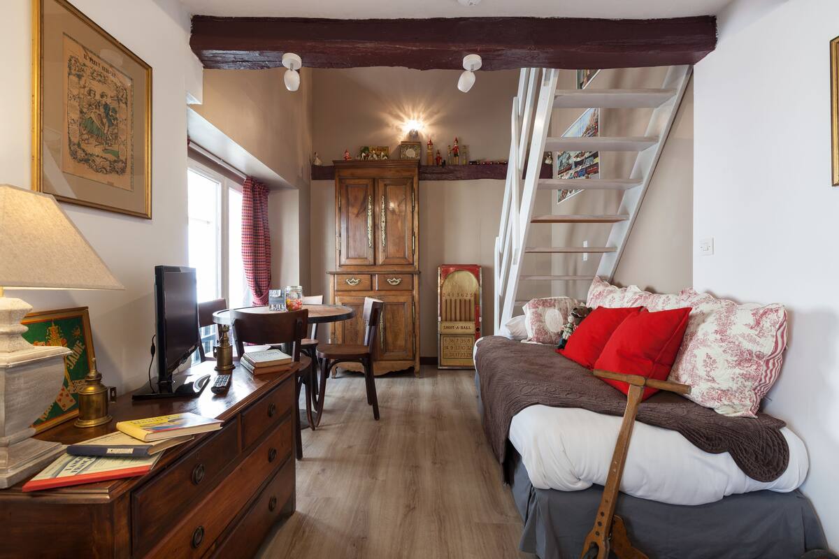 A cozy room with a wooden desk, a bed with red and white pillows, a ladder, and a wooden cabinet.
