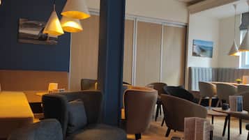 A modern restaurant interior with cushioned seating, pendant lighting, and a view of the outdoors.