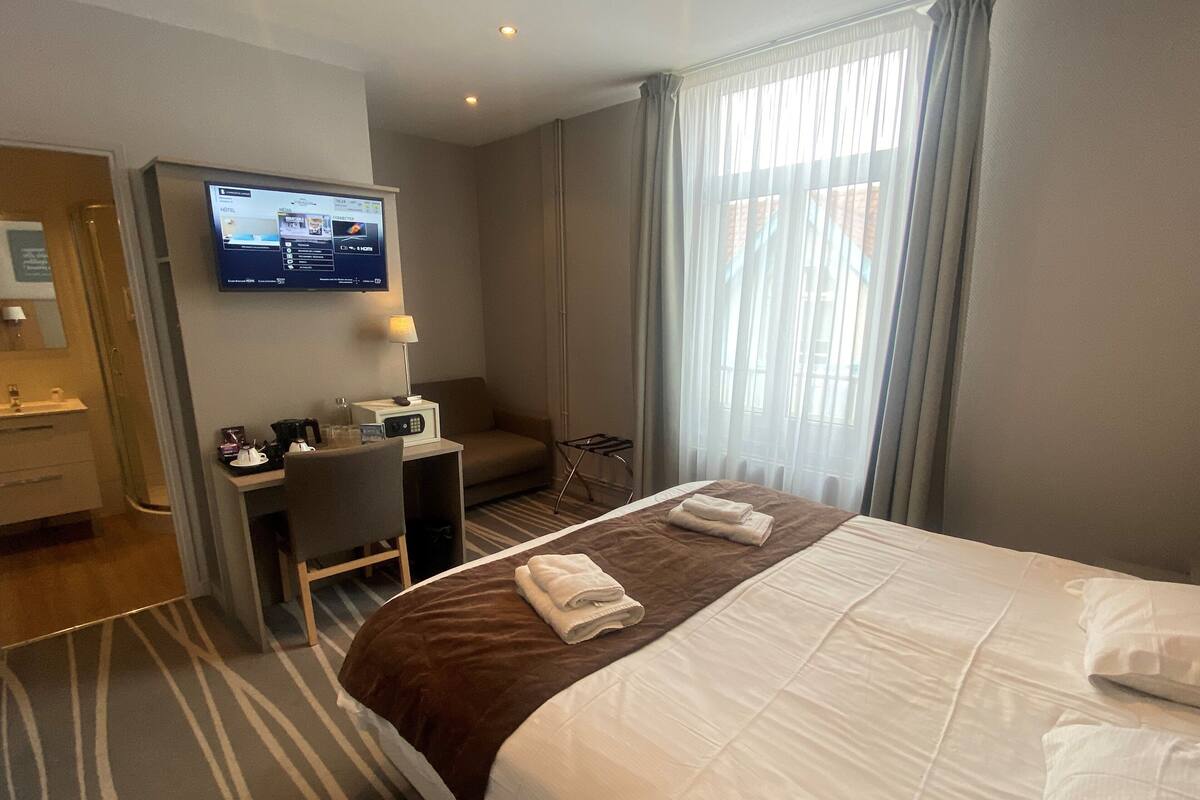 Ein Hotelzimmer mit Bett, Schreibtisch, Stuhl, Fernseher und einem Fenster mit Vorhängen.