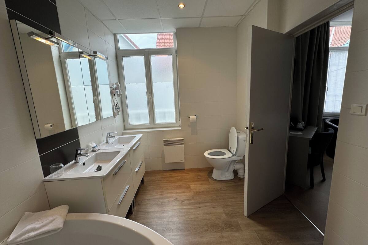 Ein modernes Badezimmer mit einer Badewanne, zwei Waschbecken, einer Toilette und einem Fenster.