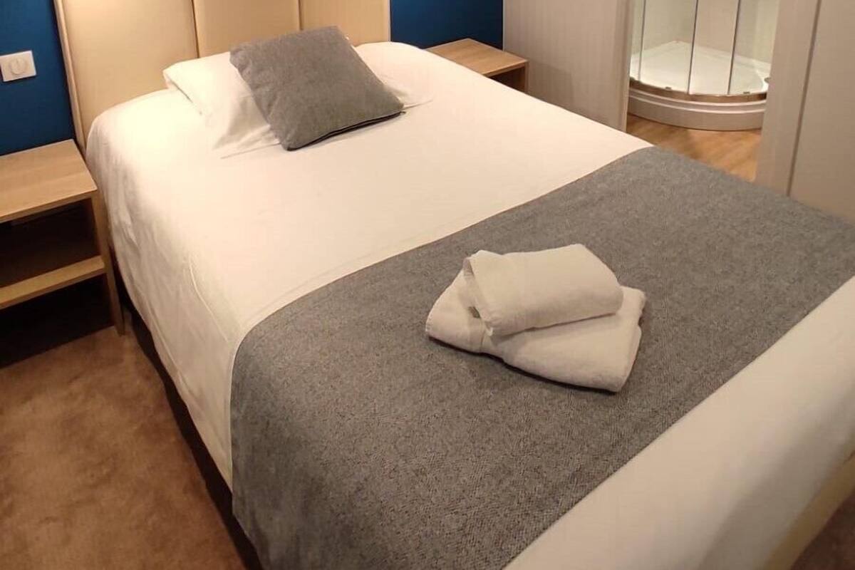 Ein Hotelzimmer mit Bett, Nachttisch, Handtuch und einer Duschkabine.