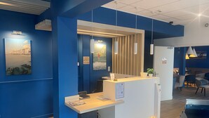 A reception desk with a blue accent wall, a wooden floor, and a modern pendant light. - Hôtel Villa Des 2 Caps (Wimereux)