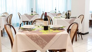 A dining area with tables set for a meal, each with a bottle of wine, glasses, and plates. - Hotel Villa Lina (Riccione)