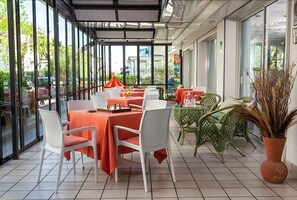 An outdoor dining area with tables and chairs, a glass enclosure, and a view of the outside. - Hotel Villa Lina (Riccione)