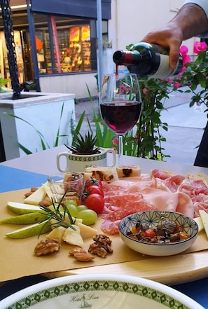 A table with a charcuterie board, a glass of red wine, and a bottle being poured. - Hotel Villa Lina (Riccione)
