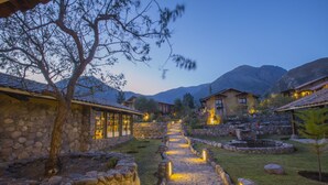 A stone pathway leading to rustic buildings with stone walls and a mountain backdrop.