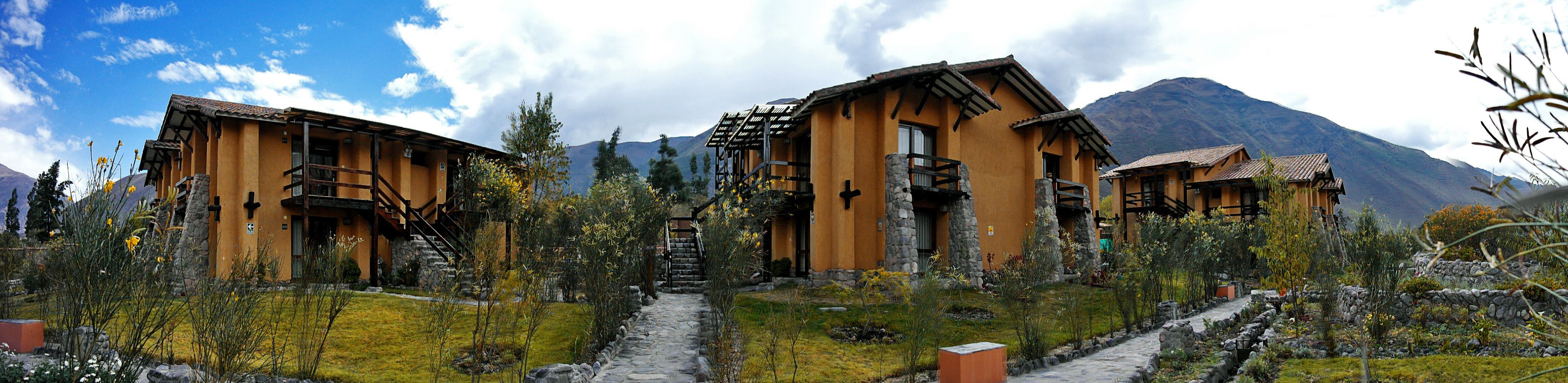 A rustic mountain lodge with stone walls and wooden beams, surrounded by a well-maintained garden and a mountain backdrop.