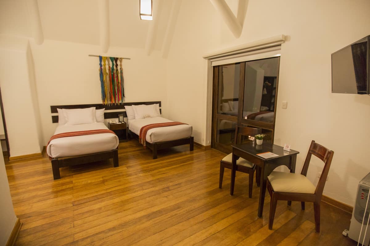 A hotel room with two beds, a desk with a chair, a small table with a plant, and a sliding door to a balcony.