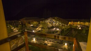 A nighttime view of a landscaped garden with a wooden deck and a stone pathway leading to a building with a sloped roof.
