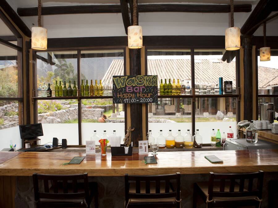 Uma área de bar com balcão de madeira, banquetas e um letreiro indicando happy hour.